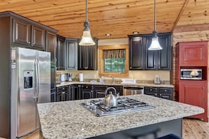 A kitchen with granite countertops, stainless steel appliances, dark cabinets, and wooden ceiling. - River Woods Retreat: Hot Tub, Hikes, 2 Fireplaces, EV (Bentonville)