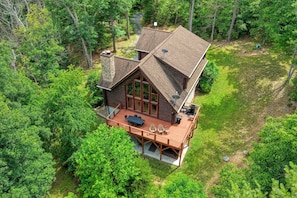 A cabin with a deck, surrounded by dense forest. - River Woods Retreat: Hot Tub, Hikes, 2 Fireplaces, EV (Bentonville)