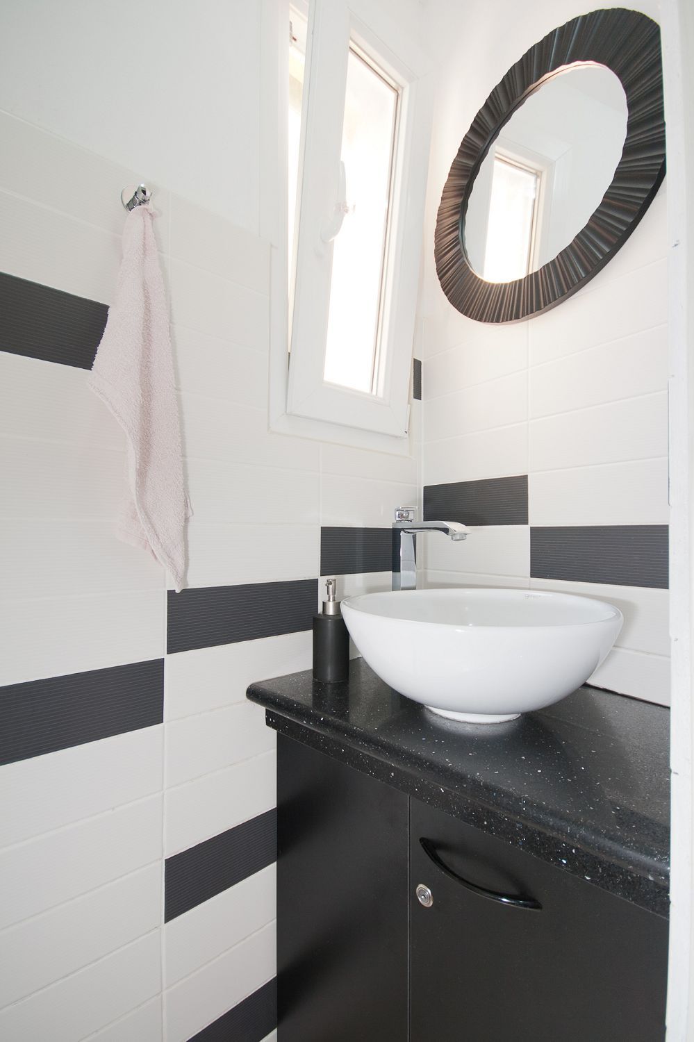 A bathroom with a white vessel sink, black countertop, and a mirror with a circular frame.