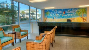 A lobby with wicker furniture, a large window, and a mural of a beach scene. - Crescent Keyes PH18-2BR/2BA Oceanfront-Pools (North Myrtle Beach)