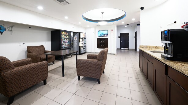 A modern living room with a dining table, two patterned armchairs, a sofa, a coffee machine, a TV, and a vending machine.
