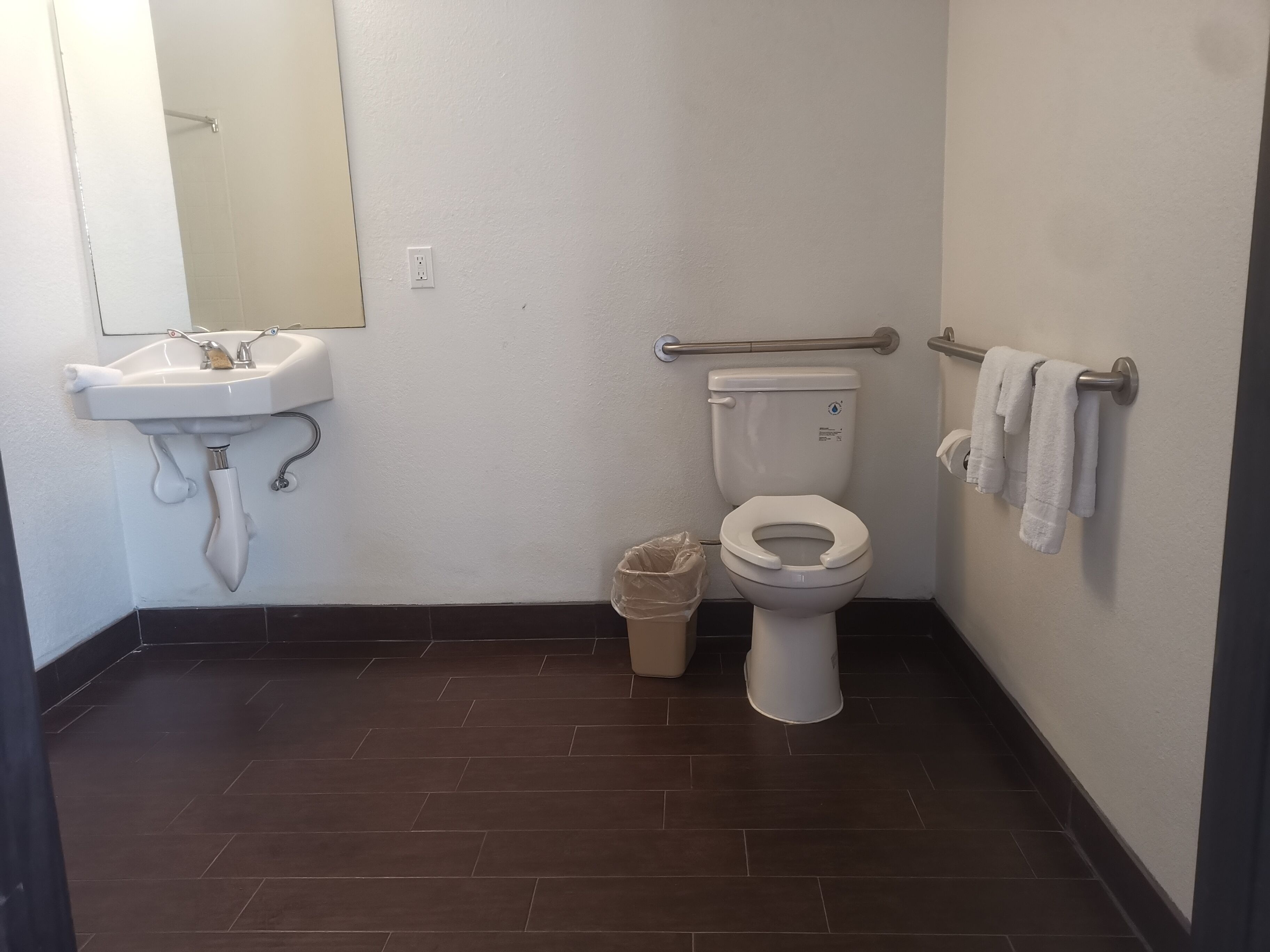 A bathroom with a white sink, toilet, and handrail.