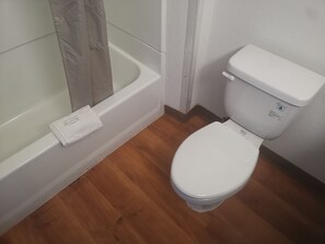 A bathroom with a white toilet, a white bathtub, and a wooden floor.