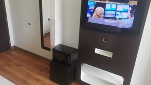 A room with a flat-screen TV mounted on a dark wall, a small black appliance, and a mirror on the wall.