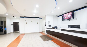 A hotel reception area with a reception desk, a television mounted on the wall, and a door leading to the room.