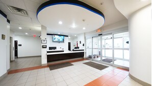 A clean, modern lobby with a reception desk, a television screen, and a glass door entrance.