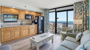 A modern kitchen with wooden cabinets, a refrigerator, and a large window overlooking the ocean.