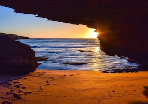 A sunset view through a cave opening with ocean waves and footprints on the sand. - Sabi@Robe - Garden Retreat - 300m from Long Beach (Robe)