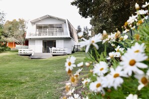 Ein zweistöckiges Haus mit Balkon, Rasen und weißen Blumen im Vordergrund.