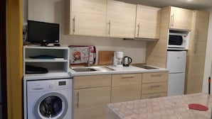 A compact kitchen with a washing machine, a microwave, a coffee maker, and wooden cabinets. - Bungalow aux Villages Sous les Pins, à 10 Minutes des Plages (LEON)