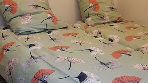 A bedroom with a bed featuring a floral bedspread, two wall-mounted hooks, and a power outlet. - Bungalow aux Villages Sous les Pins, à 10 Minutes des Plages (LEON)