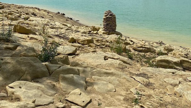 Una costa rocosa con agua turquesa cristalina y una colina boscosa a lo lejos.