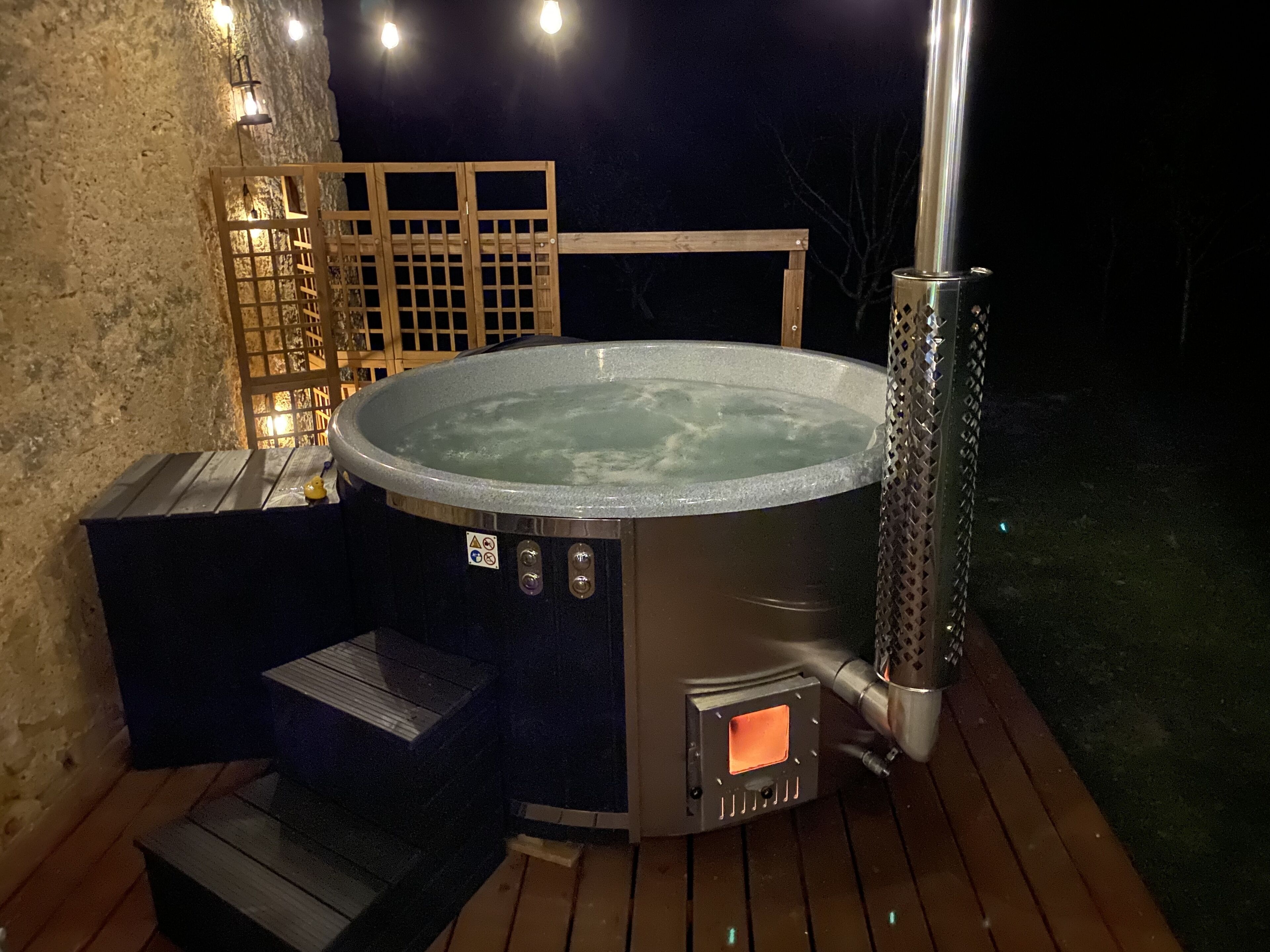 A hot tub on a wooden deck with a stone wall and a wooden fence in the background.