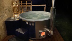 Un jacuzzi en una terraza de madera, con un muro de piedra y una valla de madera al fondo.