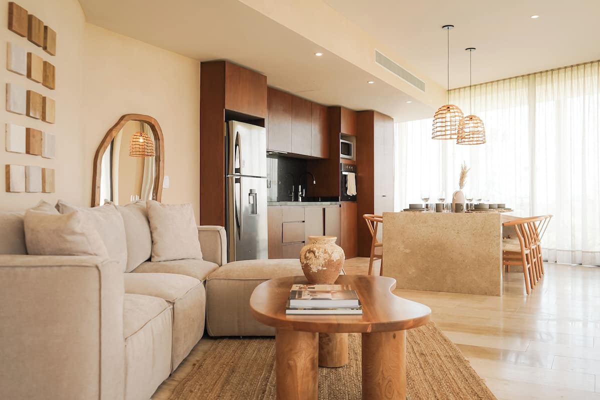 A modern living room with a sofa, a wooden coffee table, and a kitchen in the background.