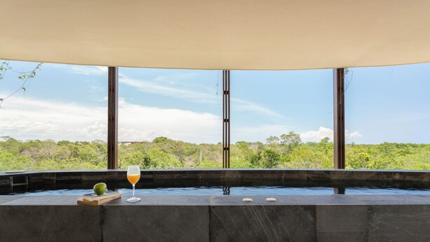 Un área de spa moderna con un ventanal grande, una bañera de hidromasaje y un vaso de jugo de naranja.
