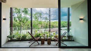 Un balcón moderno con puerta de cristal, dos taburetes y dos sillas de madera.