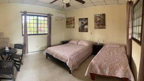 A bedroom with a bed, bedside tables, a desk with chairs, a window with curtains, and wall art. - Resting cabin with a unique garden, swimming pool and Panamanian traditions. (Guararé)