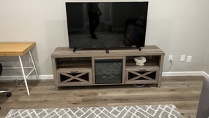 Een houten tv-meubel met een flatscreen televisie, een klein kastje en een stopcontact op de muur.