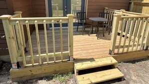 Een houten terras met een tafel en stoelen, een deur en een klein buitenruimte met een houten omheining.
