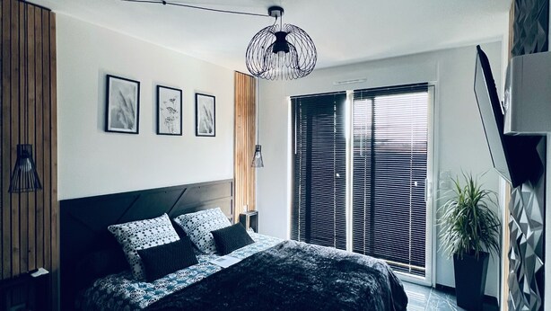Une chambre moderne avec un grand lit, un luminaire suspendu et une vue sur l’extérieur grâce à une porte coulissante.