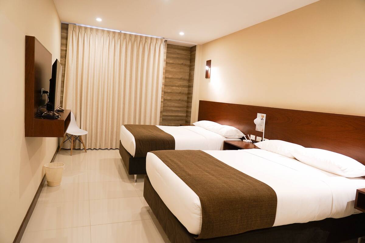 A hotel room with two beds, a TV, a desk, and a bathroom.