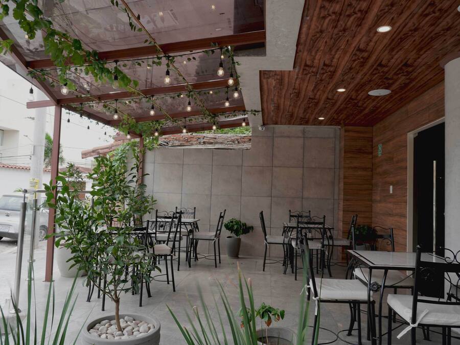 An outdoor cafe area with tables and chairs, potted plants, and string lights.