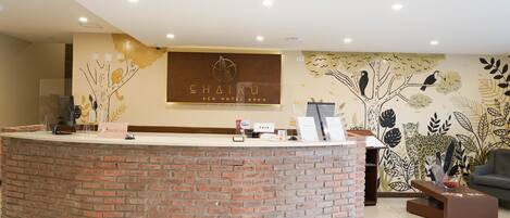 A reception area with a brick counter, a reception desk, a seating area with a sofa and a coffee table, and a wall with a nature-themed mural.