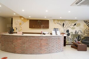 A reception area with a brick counter, a reception desk, a seating area with a sofa and a coffee table, and a wall with a nature-themed mural.