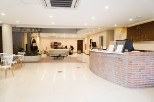 Zona de recepción de un hotel con mostrador de ladrillo, sillas blancas, un sofá y una mesa de centro.
