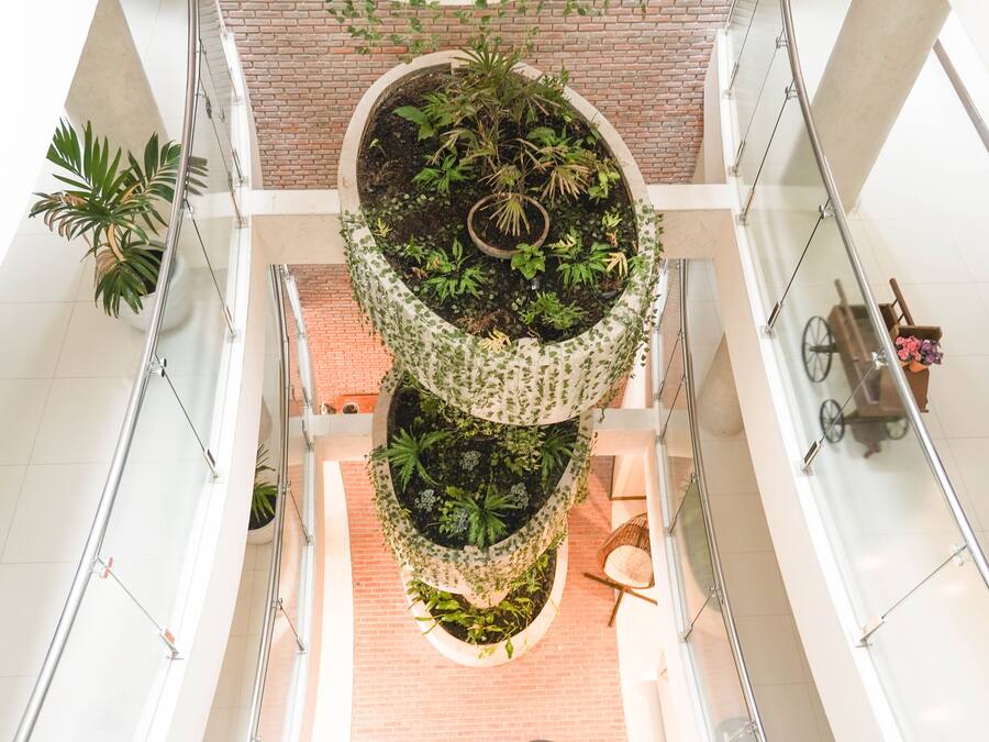 A multi-level atrium with a central planter containing various plants, surrounded by glass railings and a brick wall.