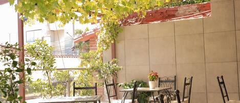 Un patio al aire libre con mesas y sillas, rodeado de plantas y un muro de ladrillo.
