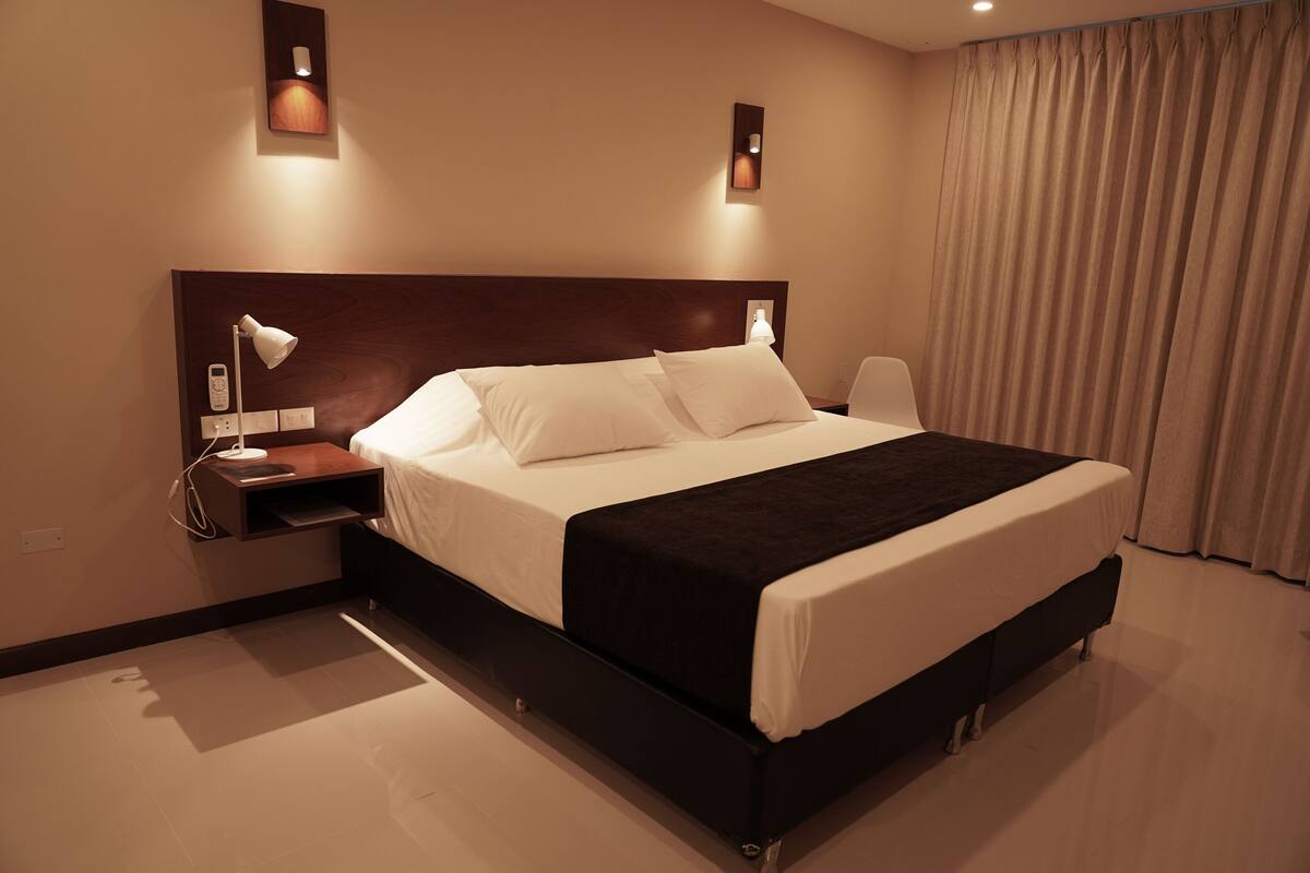 A modern hotel room with a large bed, bedside tables, and wall-mounted lamps.