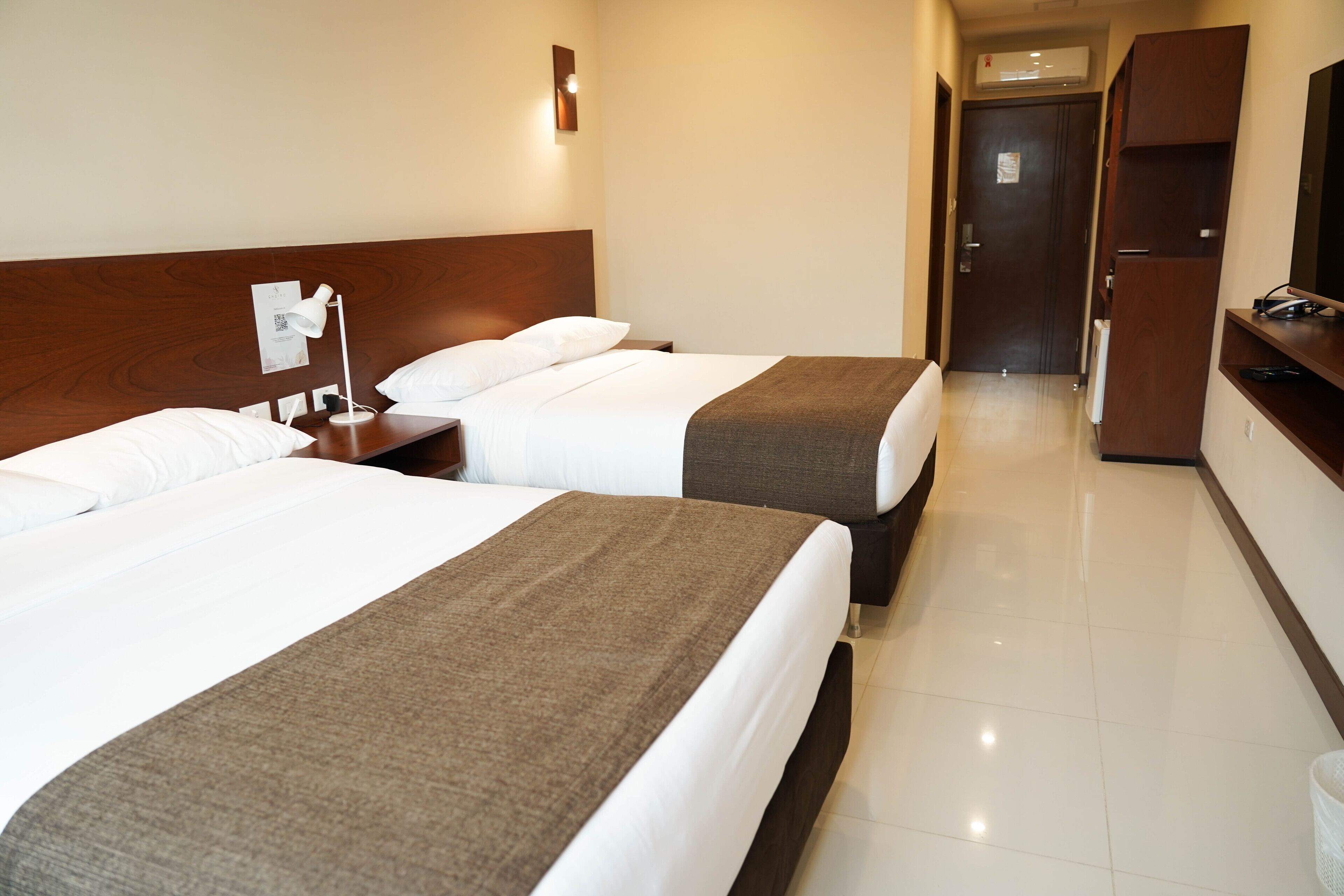 A hotel room with two beds, a desk, a chair, a TV, and a wardrobe.
