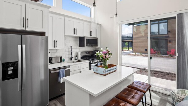 Una cocina moderna con armarios blancos, electrodomésticos de acero inoxidable y una isla central con taburetes.