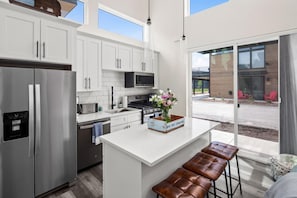 Une cuisine moderne avec des meubles blancs, des appareils en acier inoxydable et un îlot central doté de tabourets.