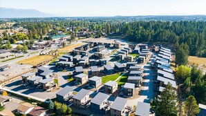 Vista aérea de una zona residencial con casas modernas dispuestas en forma de semicírculo, rodeada de bosques densos y una cadena montañosa distante.