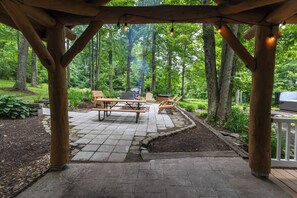 A covered patio with picnic tables and chairs, surrounded by a forested area.