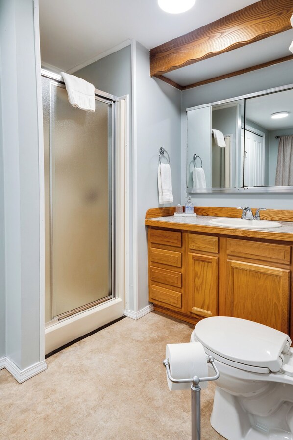 A bathroom with a glass shower enclosure, wooden vanity, and a white toilet.