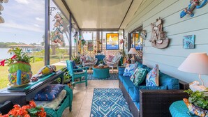 A covered porch with wicker furniture, a blue patterned rug, and various decorative items.
