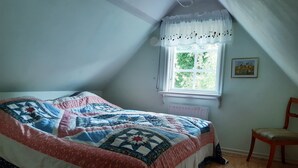 A bedroom with a large bed, a window with a view of greenery, a radiator, and a chair.