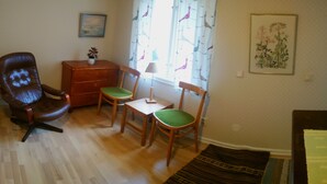 A living room with a brown leather chair, two wooden chairs with green cushions, a small wooden cabinet, a table, and a patterned rug.