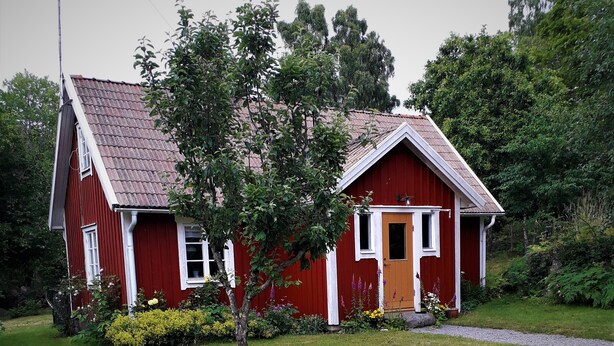 A red wooden house with a sloped roof, a front door, and a small porch.