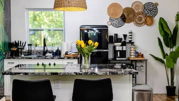 A modern kitchen with a granite countertop, black chairs, a woven pendant light, and a vase with yellow tulips.