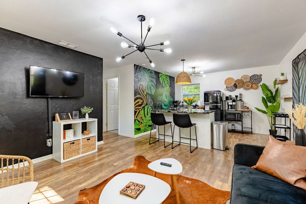 A modern living room with a flat-screen TV, a dining area with a bar, and a kitchen with a coffee machine.