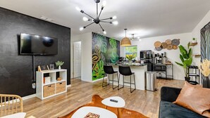 Ein modernes Wohnzimmer mit Flachbildfernseher, einer Essecke mit Bar und einer Küche mit Kaffeemaschine.