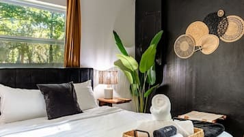 A modern bedroom with a large bed, a nightstand, a lamp, a potted plant, and a wall-mounted decorative item.