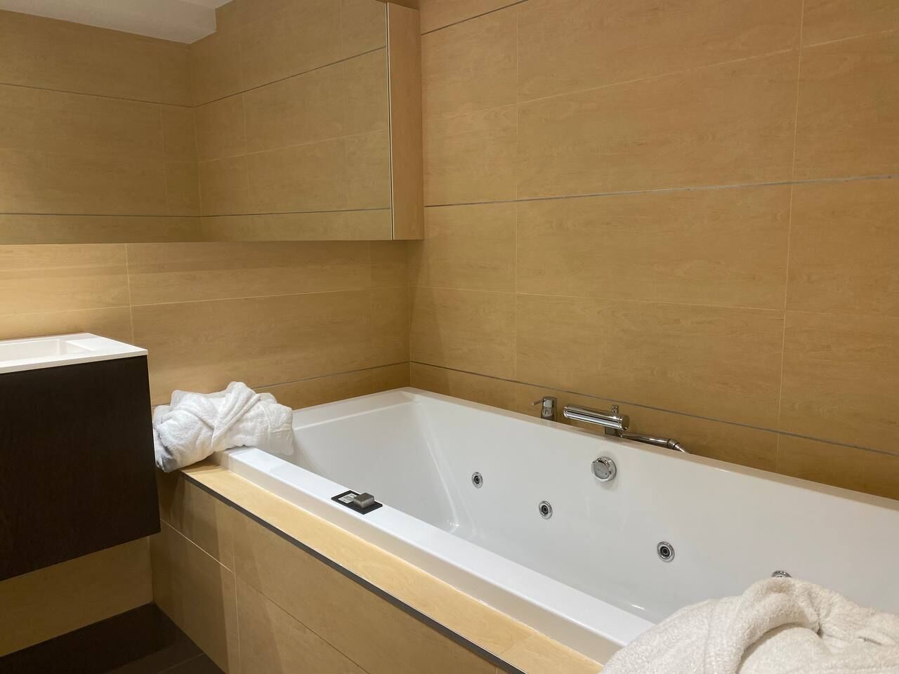 Une salle de bain moderne avec une grande baignoire, un meuble en bois foncé et des murs recouverts de carreaux beiges.