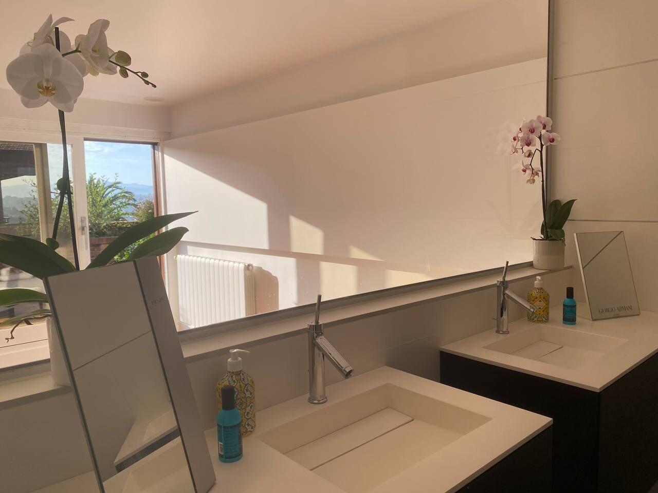 Une salle de bain moderne avec deux lavabos, un grand miroir et une orchidée en pot.