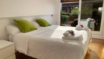 A modern bedroom with a large bed, white bedding, and green pillows. There are towels on the bed and a white nightstand to the left.